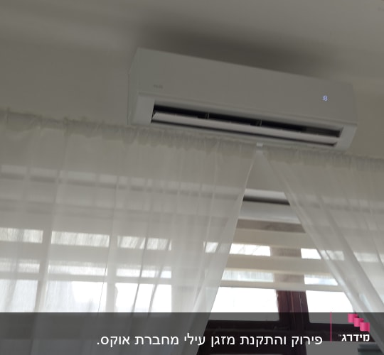 מזגן מותקן על קיר מעל חלון עם וילונות לבנים
